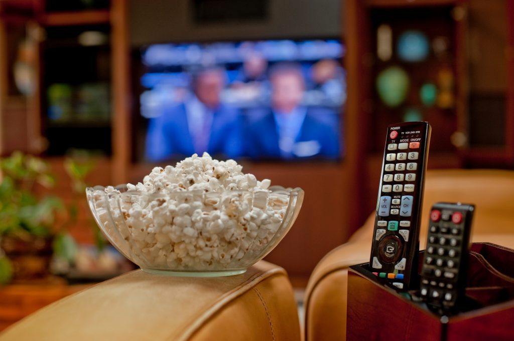 Palomitas de maíz, controles remotos y una televisión al fondo.