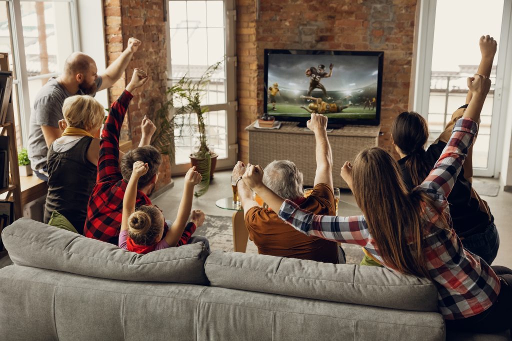 Victoria. Una familia feliz y emocionada ve un partido de fútbol americano, un campeonato en el sofá de casa. Los fanáticos aplauden emocionalmente al equipo nacional favorito. Hija, papá y abuelo. Deporte, televisión, diversión.